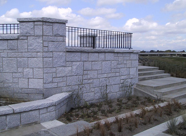 Ashlar natural stone wall with fencing on top and stairs behind